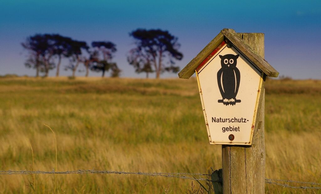 Schild für Naturschutzgebiet mit großer Eule vor einer Wiese.