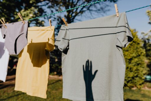 Klamotten hängen an einer Wäscheleine in der Sonne. Auf dem T-Shirt ist ein Schatten einer Hand.