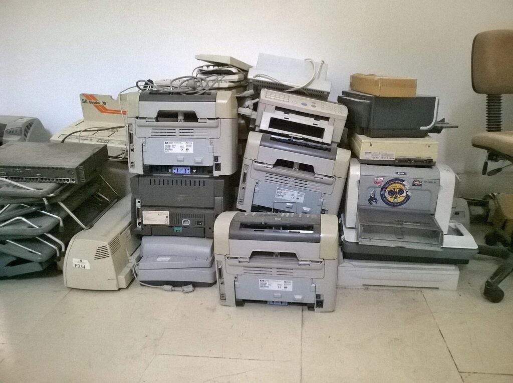 Viele alte Drucker stehen gestapelt an einer Wand.