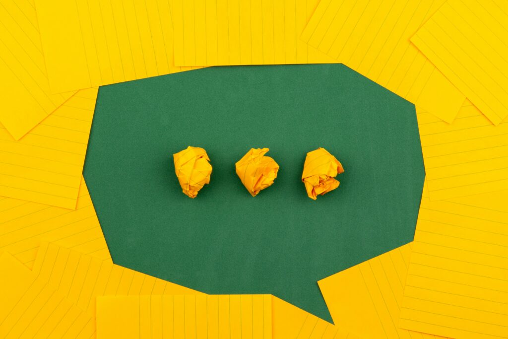 Orangefarbene Blätter liegen auf einer grünen Schultafel und bilden mit drei zerknüllten Blättern eine Sprechblase.