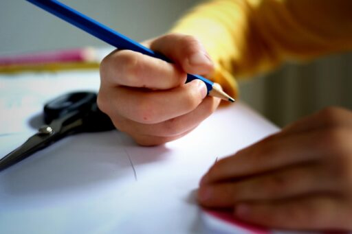 Eine Kinderhand hält einen Bleistift. Darunter ein weißes Blatt Papier.
