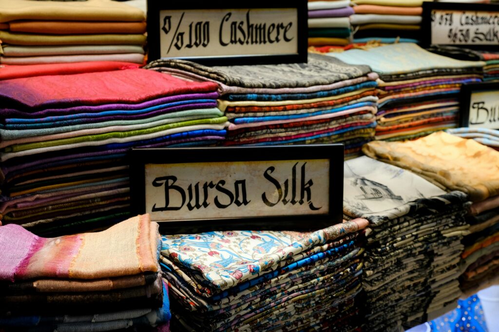 Bunte Tücher aus verschiedenem Material zu Stapel gefaltet. Ein Schild steht auf den Tüchern mit der Aufschrift "Bursa Silk"