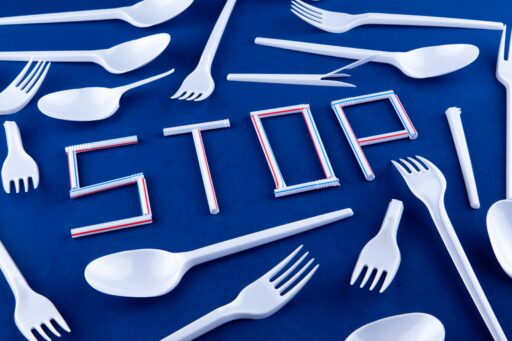 Plastik Gabel und Löffel liegen auf einem blauen hintergrund. In der Mitte steht mit Plastikstrohalmen das Wort STOP geschrieben.