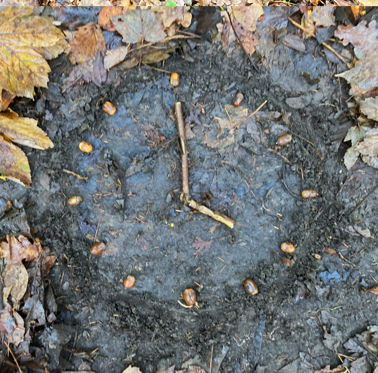 Bild einer Uhr gelegt aus Eicheln und Stöckern auf dem Erdboden