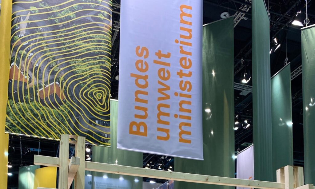 Zwei große Banner aus Stoff hängen von der Decke. Auf einem steht in großen Buchstaben: Bundesumweltministerium.