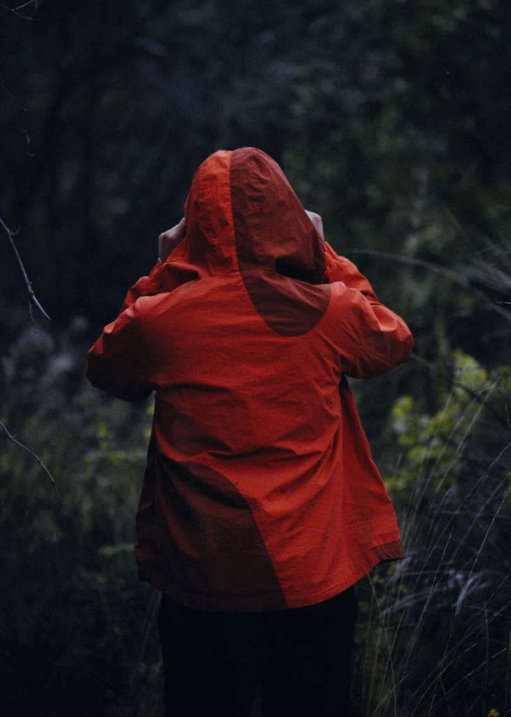 Ein Mensch von hinten mit roter Regenjacke und aufgesetzter Kapuze.