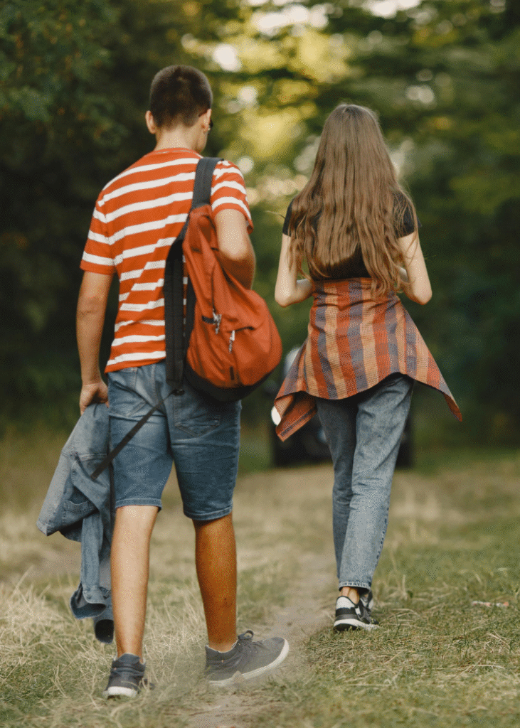 Zwei junge Menschen von hinten gehen einen Waldweg entlang.
