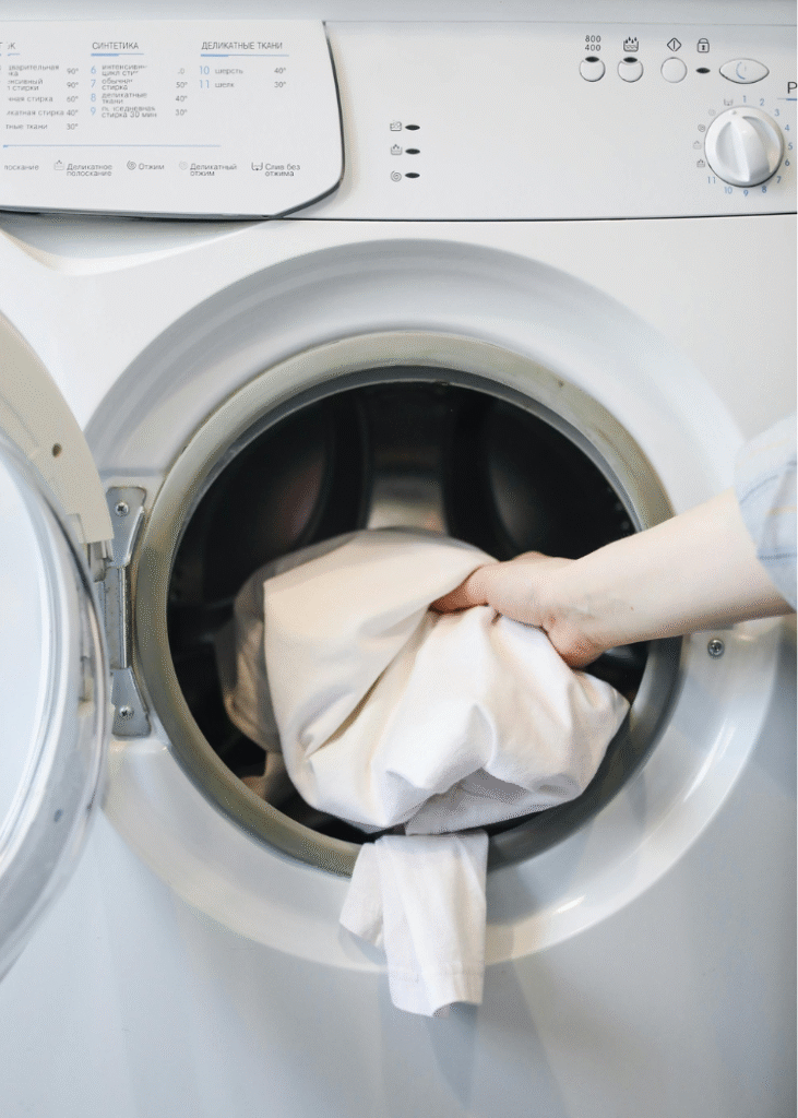 Eine Hand steckt Wäsche in eine Waschmaschine.