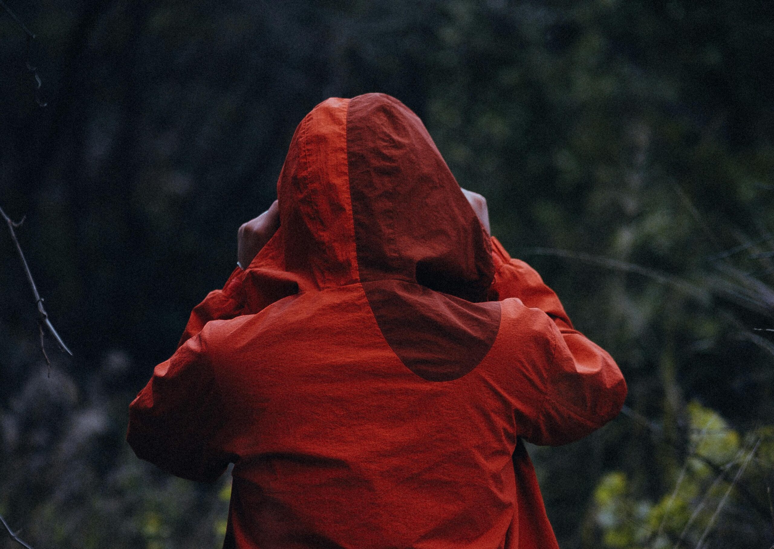 Ein Mensch von hinten mit roter Regenjacke und aufgesetzter Kapuze.