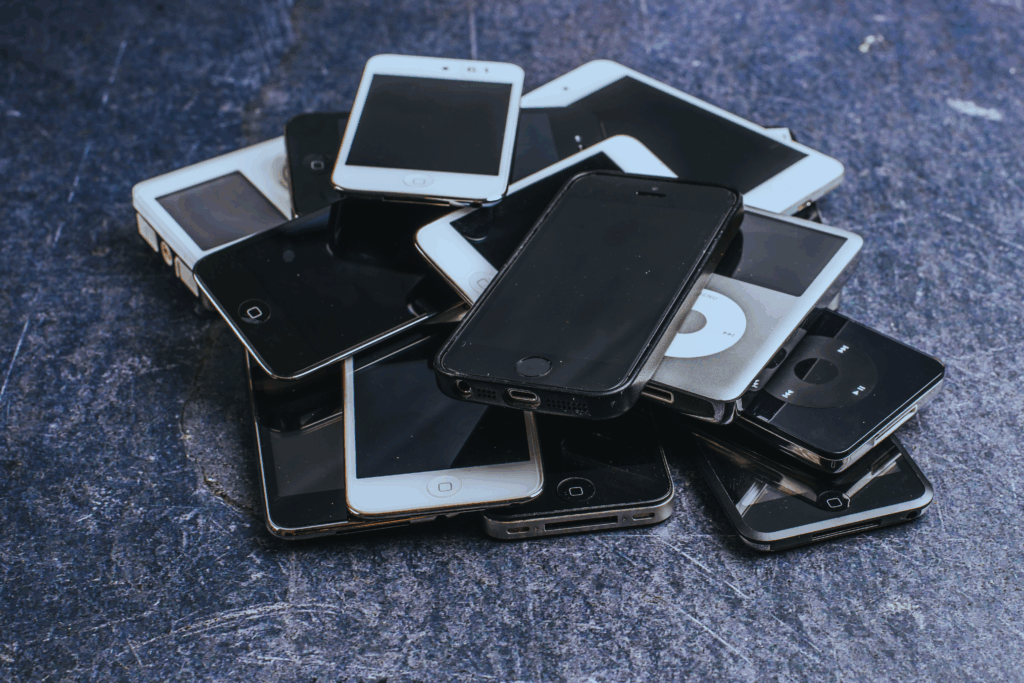 Haufen aus mehreren älteren Smartphones und MP3-Playern auf dunklem Untergrund