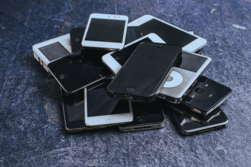 Haufen aus mehreren älteren Smartphones und MP3-Playern auf dunklem Untergrund