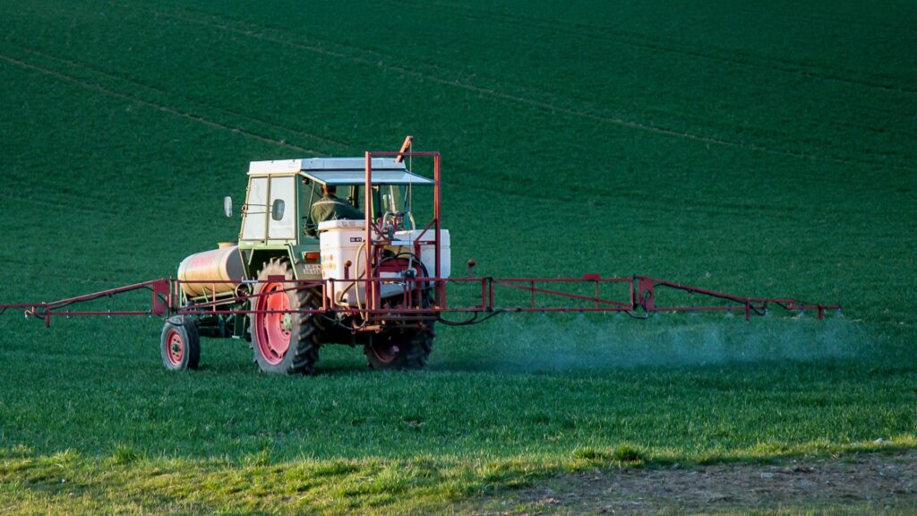 Ein Traktor auf einem großen und grünen Feld verspritzt Pestizide.
