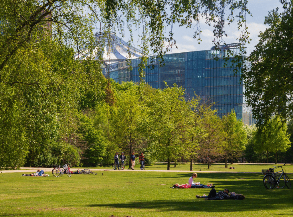 Grüne Bäume und Wiese mit Menschen im Tiergarten in Berlin im Sommer. Im Hintergrund der Potsdamer Platz.