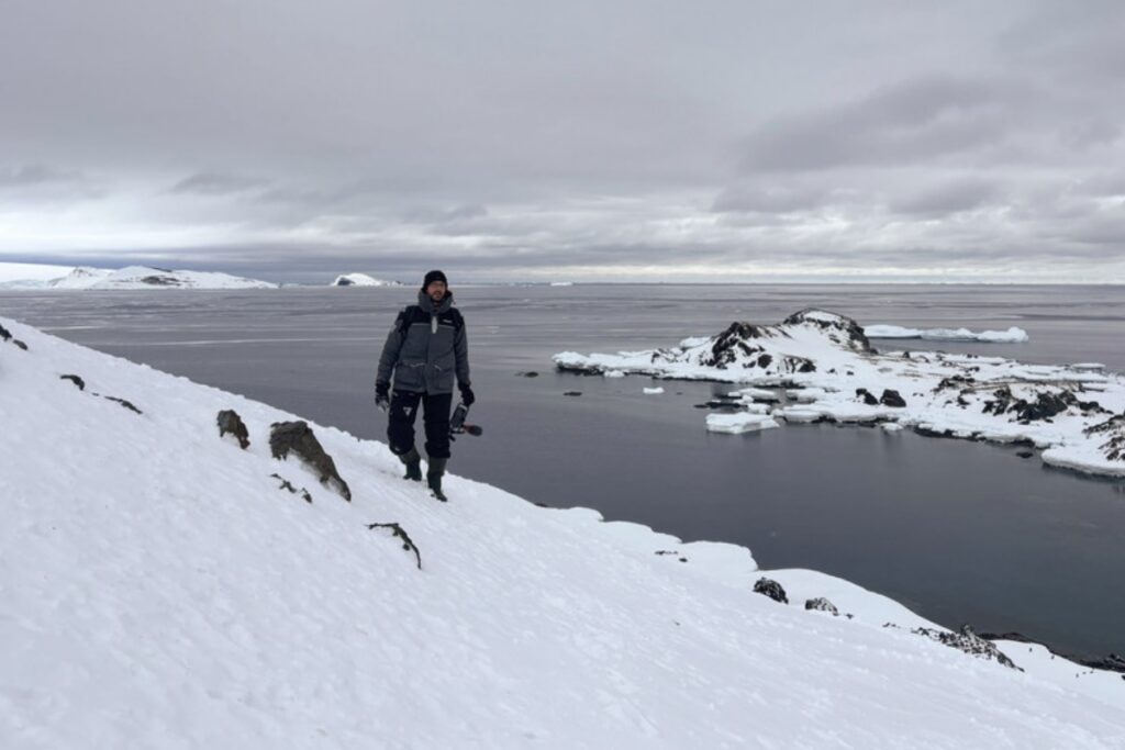 Ein Journalist läuft mit einer Kamera in der Hand über eine Schneefläche in der Antarktis.